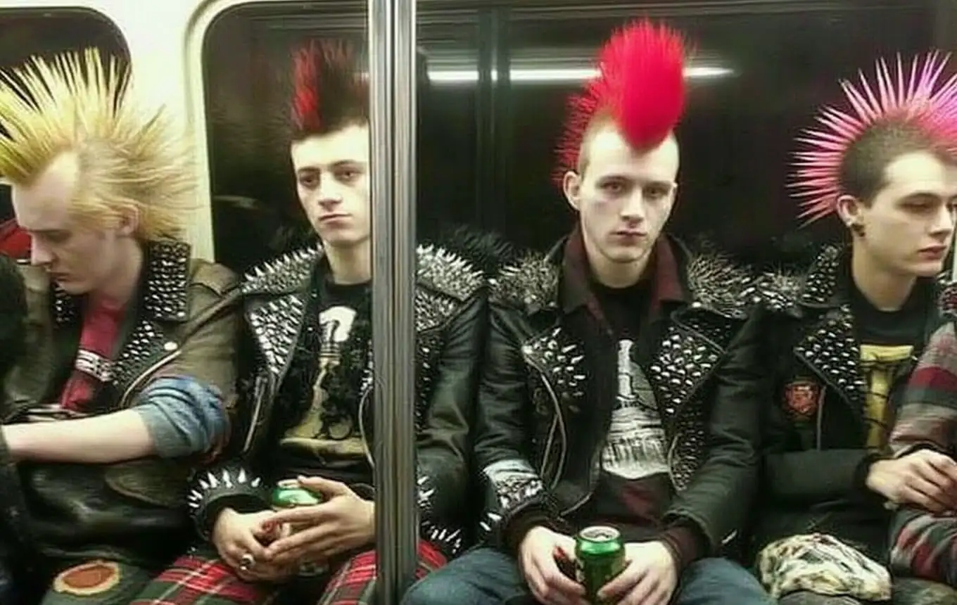 Four young punk rockers sitting on a subway, wearing spiked leather jackets and sporting colorful mohawks in yellow, red, and pink/purple.